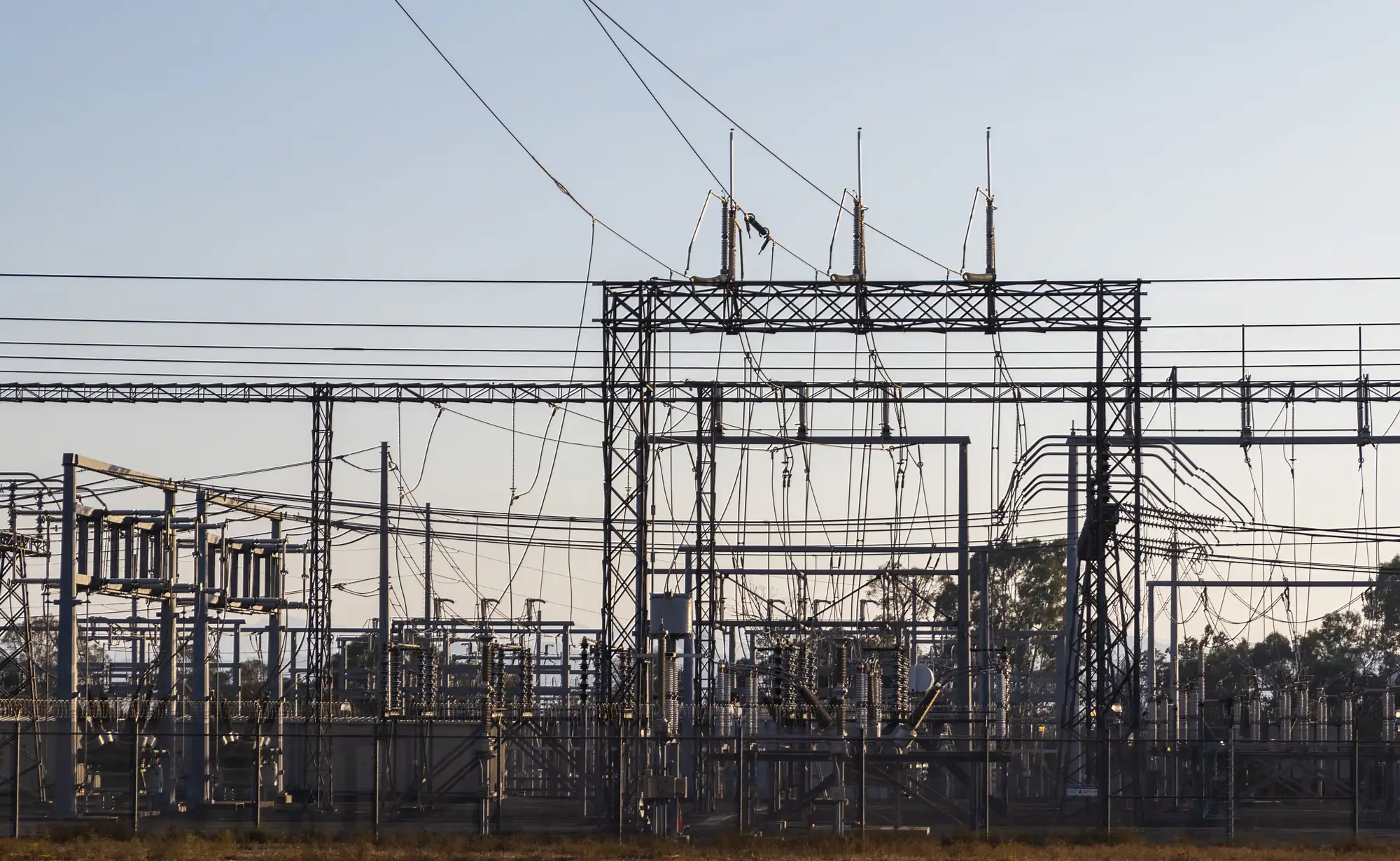 An outdoor high-voltage substation at dawn, its steel gantries and lines against a pale sky